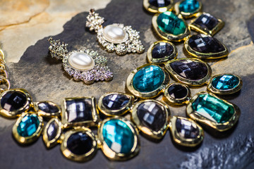 Pearl earrings and gemstones pendant, Traditional jewelry. Beautiful vintage female jewelry on dark stones background. Selective focus.