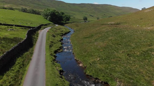 A slow aerial shot of Barbon Beck, Carnforth, Lancashire, England. This stunning countryside features a stream running alongside a small country lane.