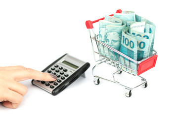 Female hand puching brazilian notes one hundred (100) reais, shopping cart or supermarket trolley and calculator and calculator, business finance shopping concept. Brazil money. © Gabriel Ramos