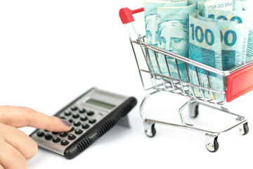 Female hand puching brazilian notes one hundred (100) reais, shopping cart or supermarket trolley and calculator and calculator, business finance shopping concept. Brazil money. © Gabriel Ramos