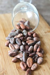 cocoa beans spilling from a glass onto a wooden surface, vegan food, igridient for healthy sweets