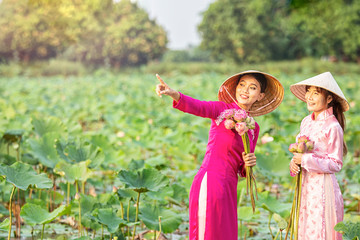 Obraz premium Vietnamese girls are inviting friends to look at the lotus flowers. Vietnamese dress with pink lotus flowers. Female boating on lakes harvest water lilies.