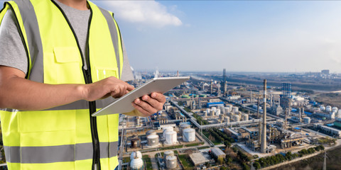 worker working on pad with oil and gas refinery background,Smart factory concept.