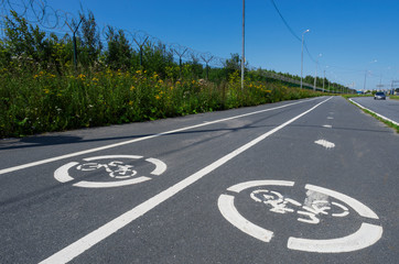 Two road signs "Bicycle path" on the asphalt and white lines close-up in the background of the blue sky