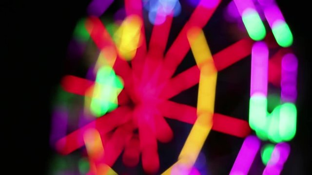 Blurred Ferris Wheel with colorful lighting decoration rotates slowly at night fun fair