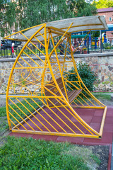 City Park in summer, empty wooden swing with yellow decorative metal frame, outdoor leisure furniture, vertical frame