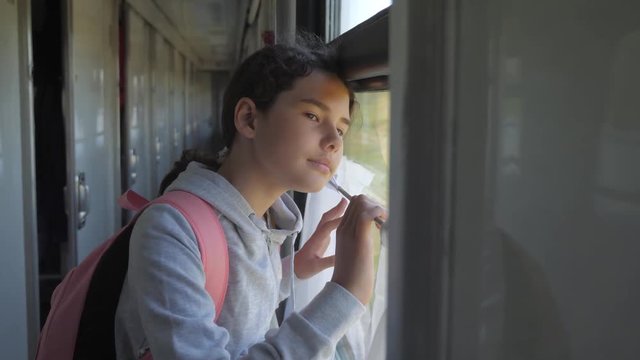 little girl teenage is backpacker traveling by train. travel transportation railroad concept. tourist school girl in the train wagon with backpack looking out the window waving his lifestyle hand