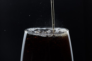 A glass of cola beverage with a salt. On a black background.