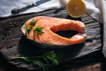Raw salmon steak on wooden cutting board with with bell pepper and dill.