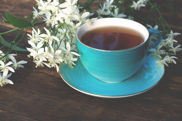 Cup of hot tea and blooming white flowers on a brown wooden table background.