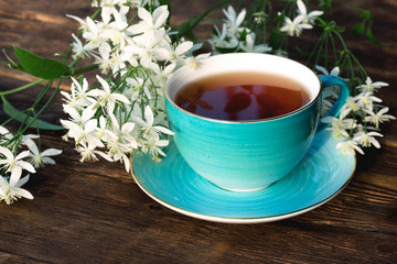 Cup of hot tea and blooming white flowers on a brown wooden table background.