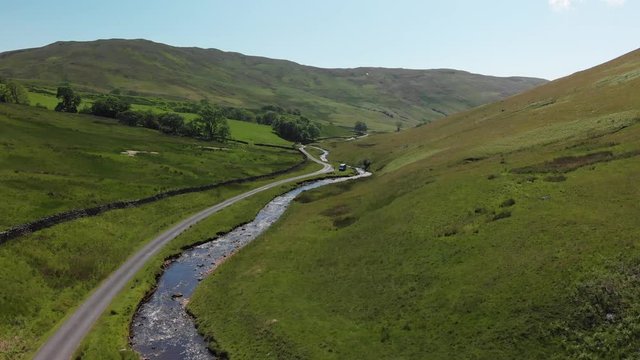 An ascending shot of Barbon Beck Valley, Carnforth, Lancashire, England. This stunning countryside features a stream running alongside a small country lane.