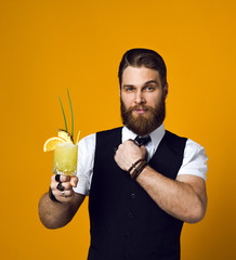 bearded barman with beard holding cocktail in waistcoat - obrazy, fototapety, plakaty