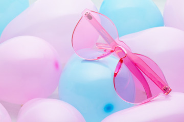 Top view of pink trendy sunglasses over the pastel background made with pink and blue balloons