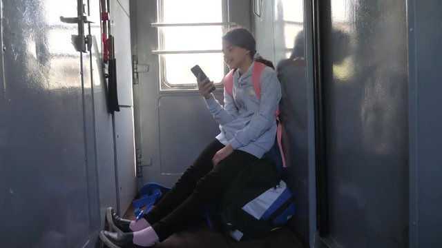 Teenager girl traveler with a backpack sitting on bags backpacks at the window of the car with a smartphone. Travel rail carriage concept. the girl in the train at the window corresponds to the girl