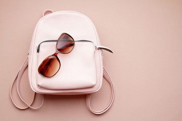 Flat lay with pink woman accessories  with backpack and woman hand holding the sunglasses. Summer fashion trends, shopping idea