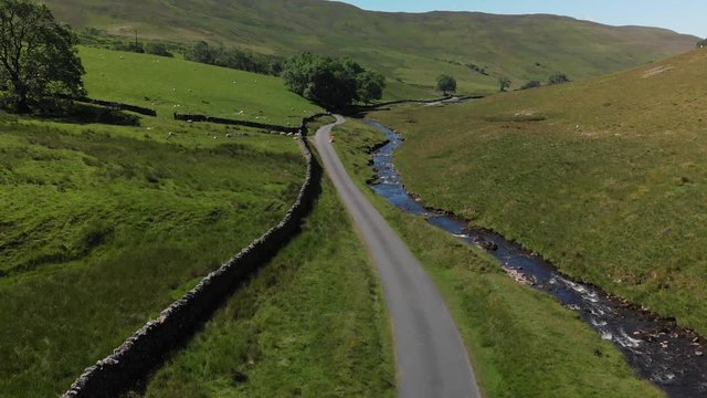 An ascending aerial shot of Barbon Beck, Carnforth, Lancashire, England. This stunning countryside features a stream running alongside a small country lane.