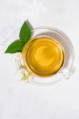 glass cup with green tea on a white background and a branch of jasmine, vertical top view