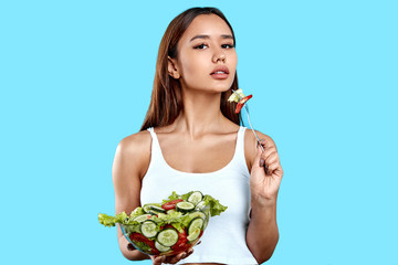 tanned sportswoman eating salad with a fork. girl leads healthy lifestyle, close up photo. isolated...