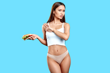 slim sexy girl holding burger, doesn't want to eat it as it has many callories. close up photo....