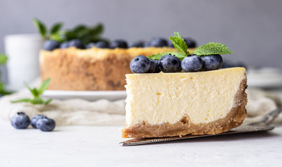 New York style cheesecake, fresh blueberries and mint on a white plate. Light stone background. Copy space.