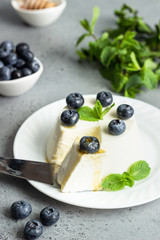 Italian ricotta cheese on a white plate with fresh blueberries, mint and honey on grey background. Selective focus, copy space. 