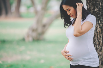 Portrait of asian Beautiful pregnant woman at the park,Thailand people,Happy woman concept,Her use hand touch her belly,Mother day concept