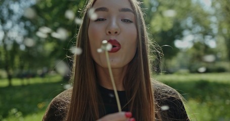 Young spring fashion woman blowing dandelion in spring garden. Springtime. Trendy girl at sunset in spring landscape background. Allergic to pollen of flowers. Spring allergy