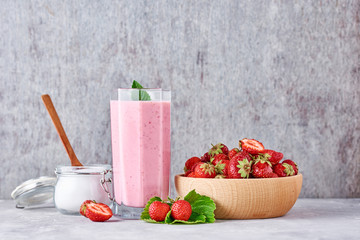 Strawberry smoothie in glass jar and fresh strawberries in wooden bowl on a gray background