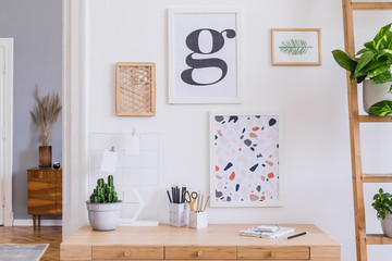 Stylish and design home interior of office room with wooden desk, office supplies, mock up poster frames, cacti, plants and elegant accessories. Modern and minimalistic home decor. Template. 