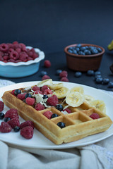 Waffles with fresh banana, raspberries, blueberries for breakfast. Belgian waffles. Dark wooden background.