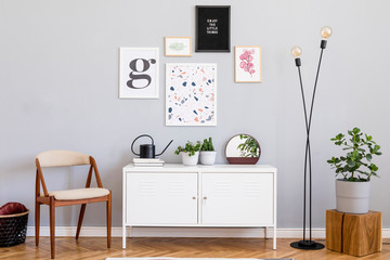 Design scandinavian home interior of open space with mock up posters gallery wall, white shelf, chair, plants, lamp and elegant accessories. Gray background walls. Retro cozy home decor. Template.