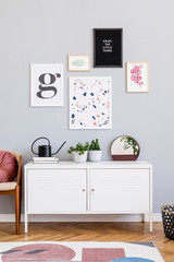 Design scandinavian home interior of open space with mock up posters gallery wall, white shelf, chair, plants and elegant accessories. Gray background walls. Retro cozy home decor. Template.