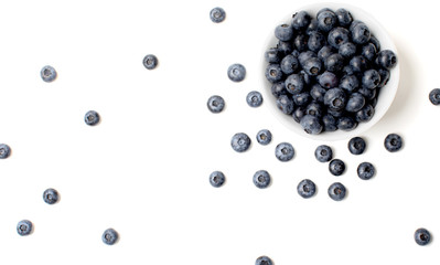 Blueberry berry in a white bowl and scattered around on a white background isolated