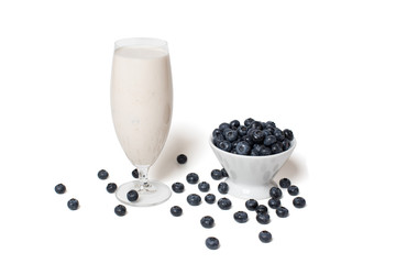 Fototapeta na wymiar Blueberries in a white bowl and scattered around a glass of milkshake on a white background isolate