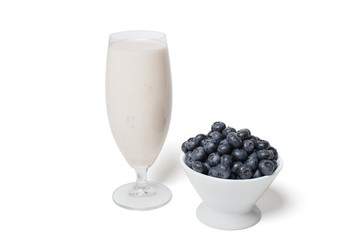 Blueberries in a white bowl and scattered around a glass of milkshake on a white background isolated