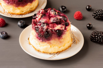 Delicious cottage cheese casserole with berries, cottage cheese pudding with berries. Appetizing fresh cottage cheese casserole with blueberries, raspberries and blackberries on a  gray background.