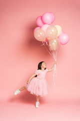 Happy celebration of birthday party with flying balloons of charming cute little girl in tulle dress smiling to camera isolated on pink background. Charming smile, expressing happiness