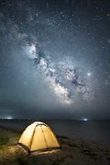 illuminated yellow tent standing at night against milky way and sea
