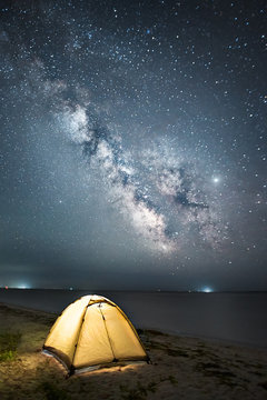 illuminated yellow tent standing at night against milky way and sea