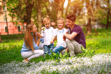 Fototapeta premium Portrait of family having fun in flowering city park on bright sunny day happily spending their leisure time together outdoors