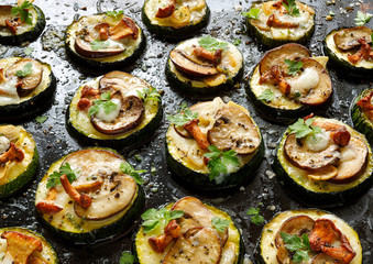 Zucchini pizza bites  from zucchini slices with the addition of brown mushrooms,  chanterelles, mozzarella cheese and herbs on a black background, close-up. Vegetarian food