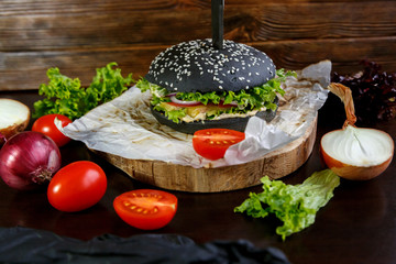 Black burger with tomatoes, with Chinese cabbage, onions on a black wooden background