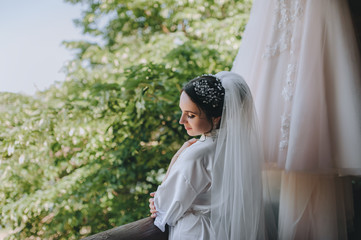 The blonde bride sits on a white bed with a bouquet and smiles sweetly. Wedding interior. Charges...