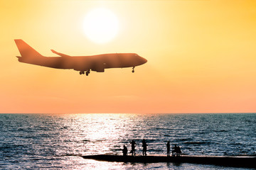 Fototapeta na wymiar jet airplane flying over sea water on sunset sky background side view of passenger plane silhouette and people on ocean pier fishing air travel vacation concept evening nature landscape wallpaper