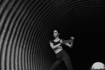 Sports woman on tunnel urban background. Fitness model working out outdoor. Young beautiful slim brunette girl doing stretching warmup exercise with resistance band. Black and white.
