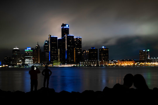 Silhouette of a man taking photo of his kid with Detroit skyline at the background