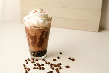 Ice coffee in the glass topped whipping cream with coffee beans. Cold summer drink on wooden background and copy space. Advertising for caramel mocha and chocolate beverage for the cafe.