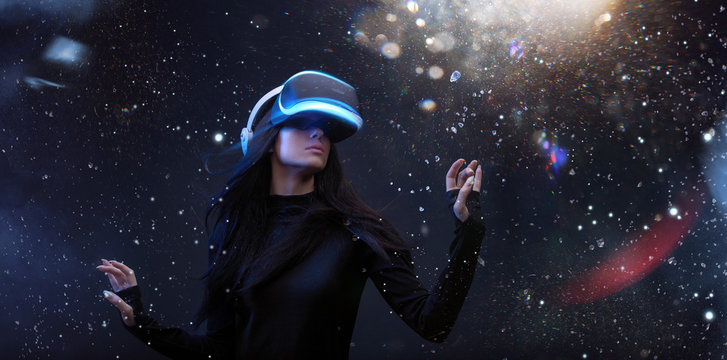 Beautiful woman with flowing hair in futuristic dress over dark magic light background. Girl in glasses of virtual reality. Augmented reality, game, future technology concept. VR.