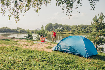 The man and the woman have a rest on the river bank with a tent - a hiking trip - a vacation in the country alone with nature